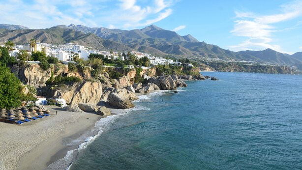 A coastal town with buildings on a cliff overlooking the sea, a sandy beach, and mountains in the background. - GREAT HOUSE IN PARADOR AREA WITH POOL AND SEA VIEWS CLOSE TO BURRIANA AND CITY (Nerja)