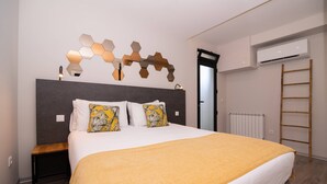 A modern hotel room with a large bed, a wooden nightstand, a wall-mounted air conditioning unit, and a ladder against the wall. - Studio north lower-level w/ kitchenett and patio (Santana)