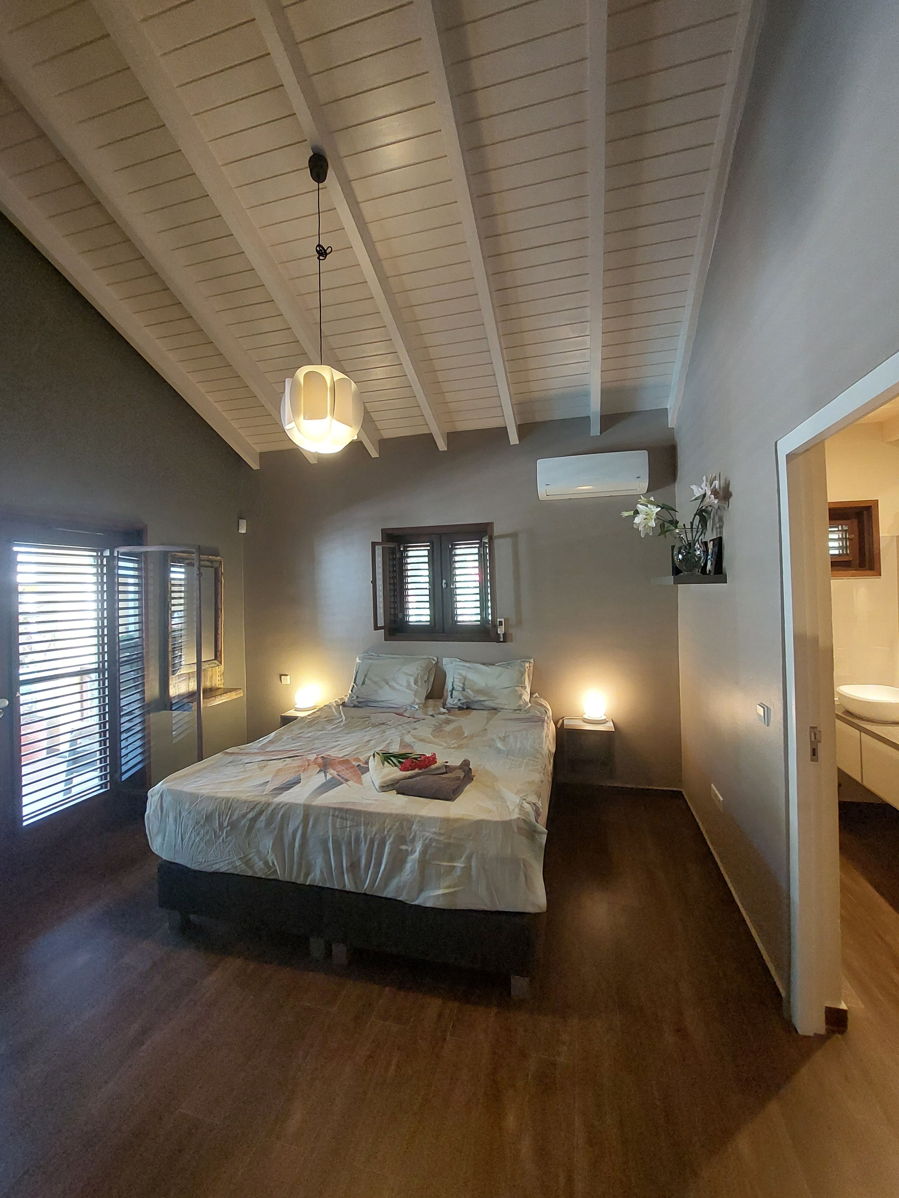A bedroom with a bed, bedside lamps, a ceiling fan, and a window with blinds.