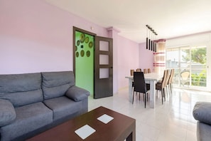A modern living room with a grey sofa, a wooden coffee table, and a dining area with a table and chairs. - House with pool, barbacue and garden, to 1500 meters from the fine sandy beach (Cubelles)