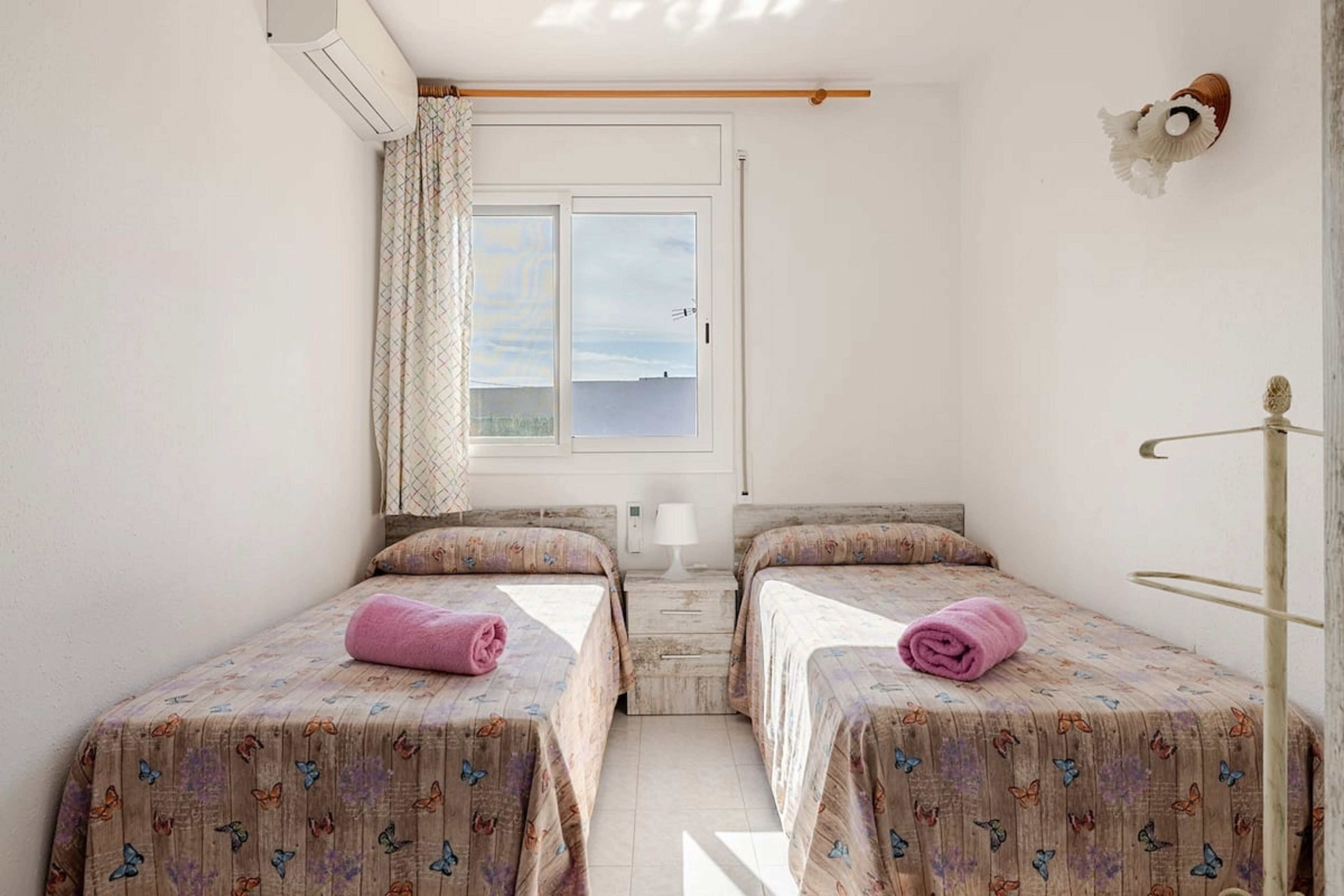 A room with two beds, a window with a view, a curtain, and a wall-mounted decoration.