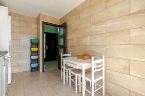 A small kitchen with a white refrigerator, a dining table with chairs, and a tiled floor.