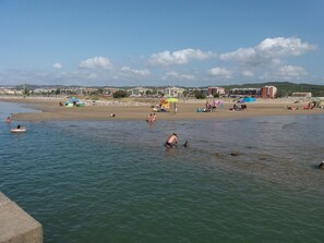 A beach with people swimming and sunbathing, umbrellas, and beach chairs.
