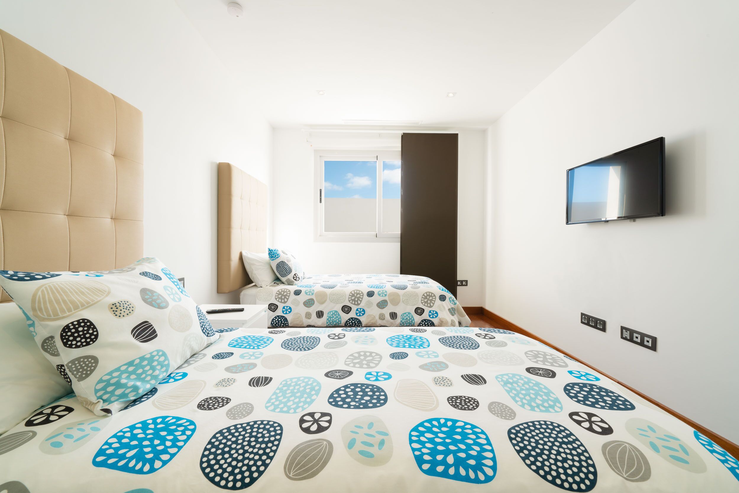 Ein Schlafzimmer mit zwei Betten, einem großen Fenster, einem Flachbildfernseher und einer Tür.