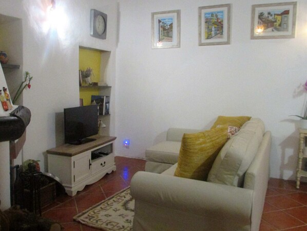 Uma sala de estar com um sofá, uma televisão em um móvel, um relógio na parede e quadros emoldurados.
