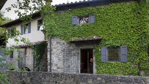 A stone building with a rustic charm, partially covered in green ivy, featuring a traditional tiled roof and a small entrance with a wooden door.