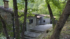 A stone building with a tiled roof, surrounded by trees and a stone staircase leading to a door.