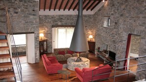 A stone-walled living room with a fireplace, red sofas, and a wooden staircase.
