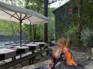 Ein Essbereich im Freien mit Feuerstelle, Tischen und Sonnenschirm.
