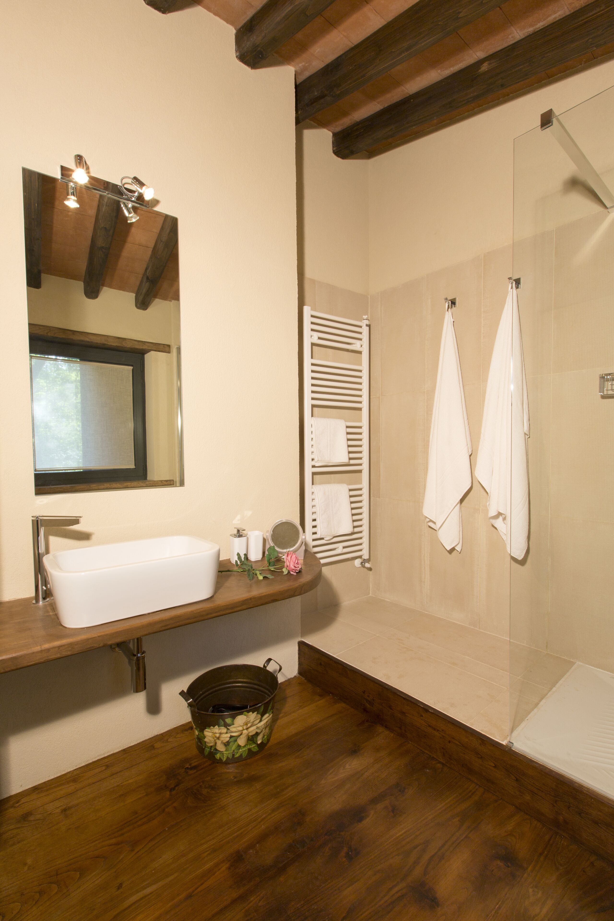 Une salle de bain avec un meuble-lavabo en bois, un grand miroir, une baignoire et un espace douche.