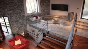 A stone-walled room with a fireplace, a red sofa, and a staircase leading to a lower level.