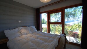 A bedroom with a large bed, wooden walls, and a window with a view of trees and a building.