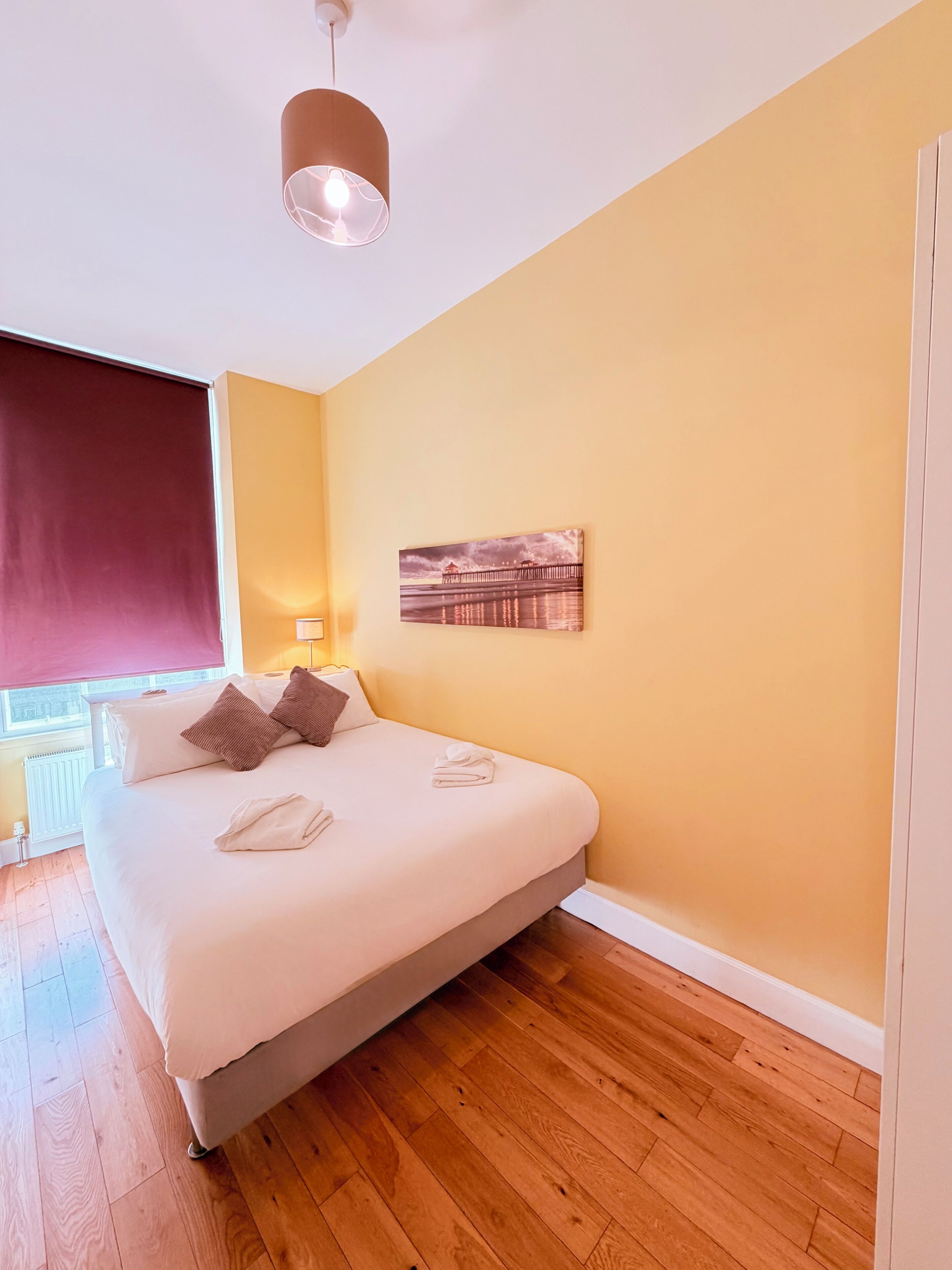 Ein Hotelzimmer mit Bett, Gemälde, Lampe und einem Fenster mit Jalousie.