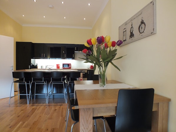 A modern kitchen with black cabinets, a wooden dining table, and a vase of tulips.