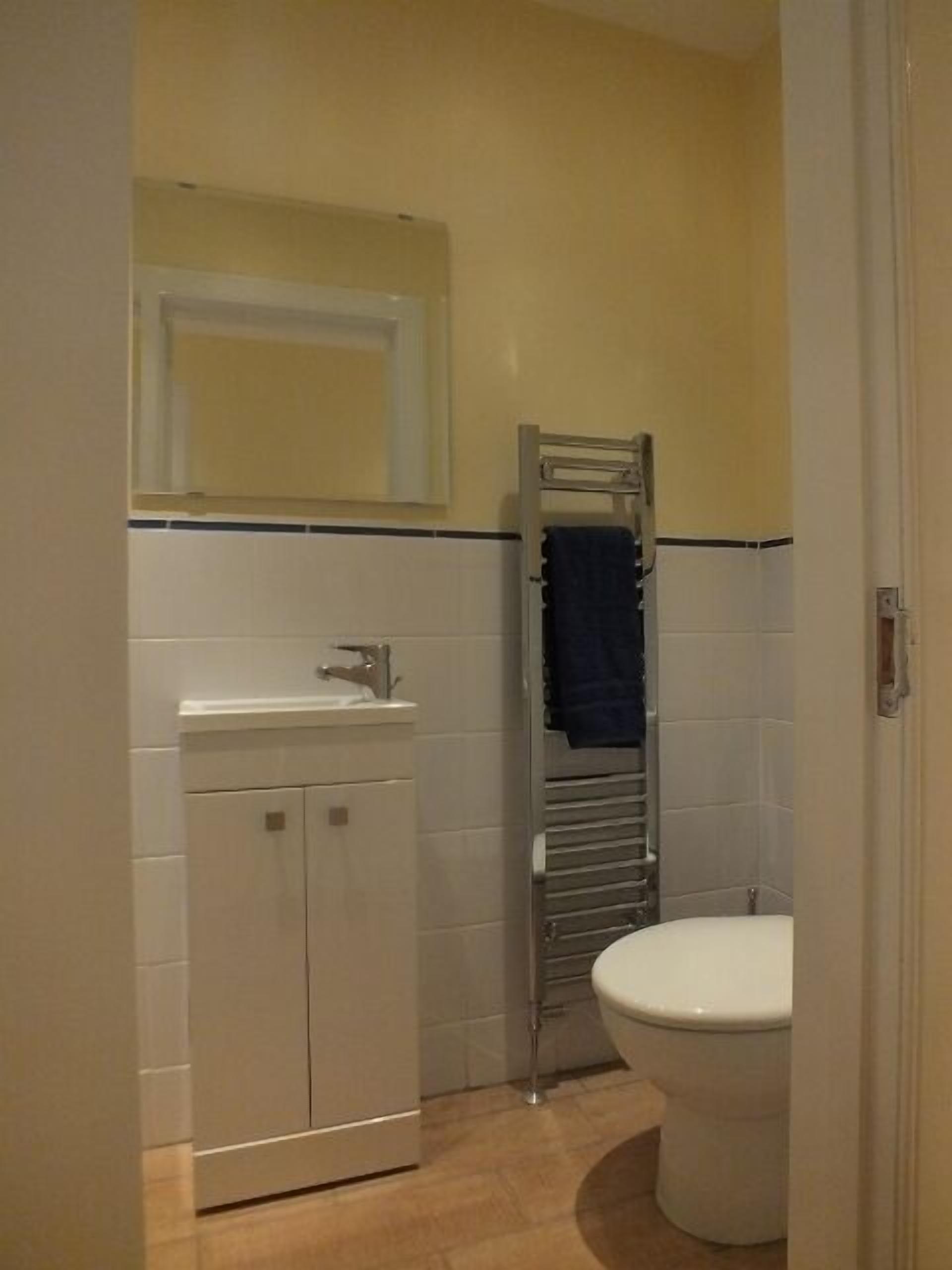 A bathroom with a white sink, a mirror above it, a towel rack with a blue towel, and a white toilet.