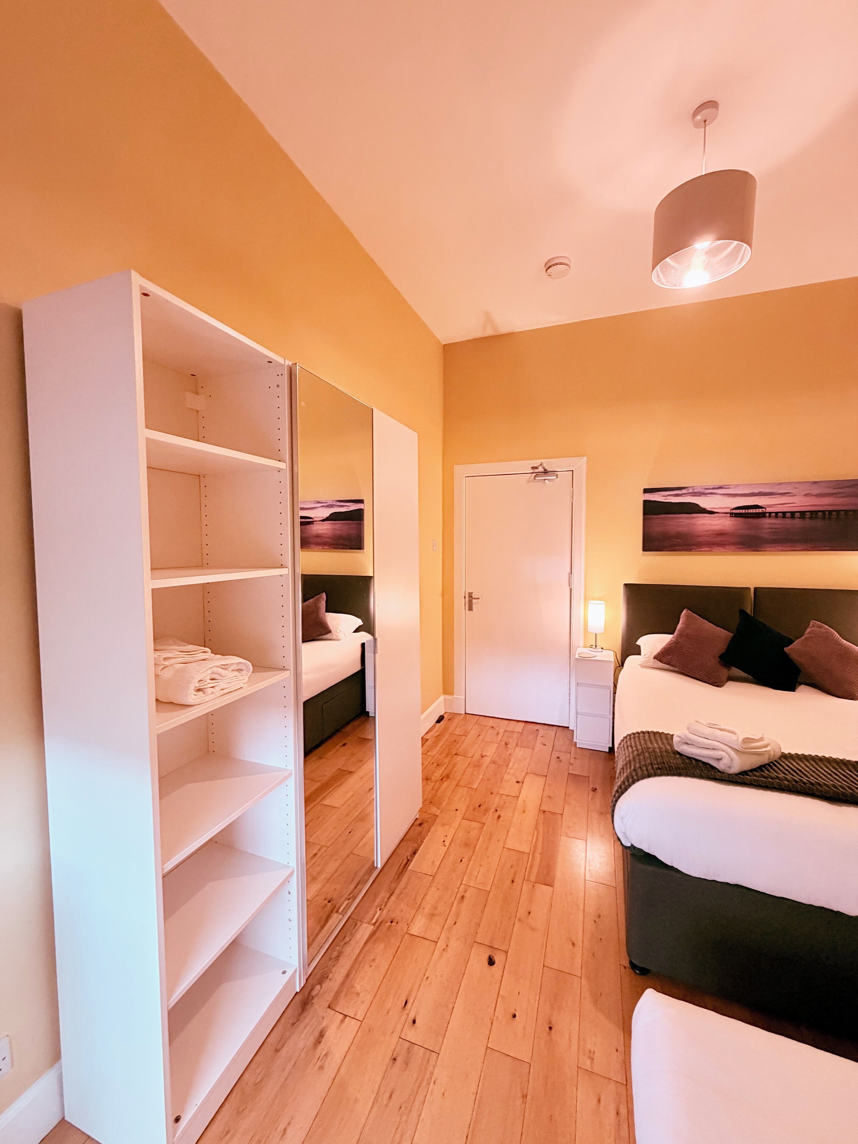 A hotel room with a bed, a wardrobe, a nightstand, and a painting on the wall.