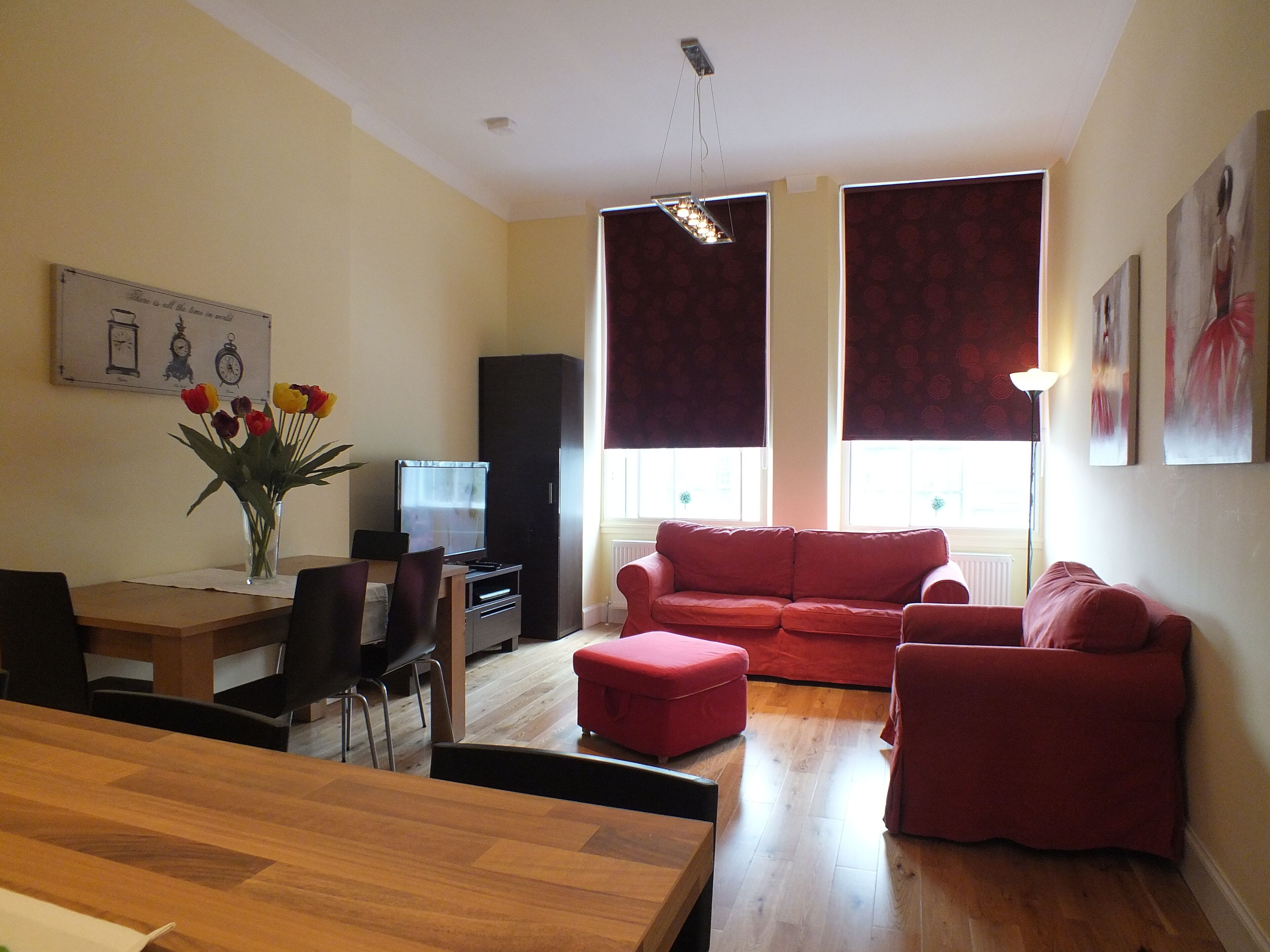 Una sala de estar con una mesa de comedor de madera, sofás rojos, un televisor y un jarrón con flores.