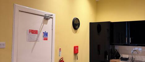 A kitchen with wooden flooring, a white door, a red fire extinguisher, and black cabinets.