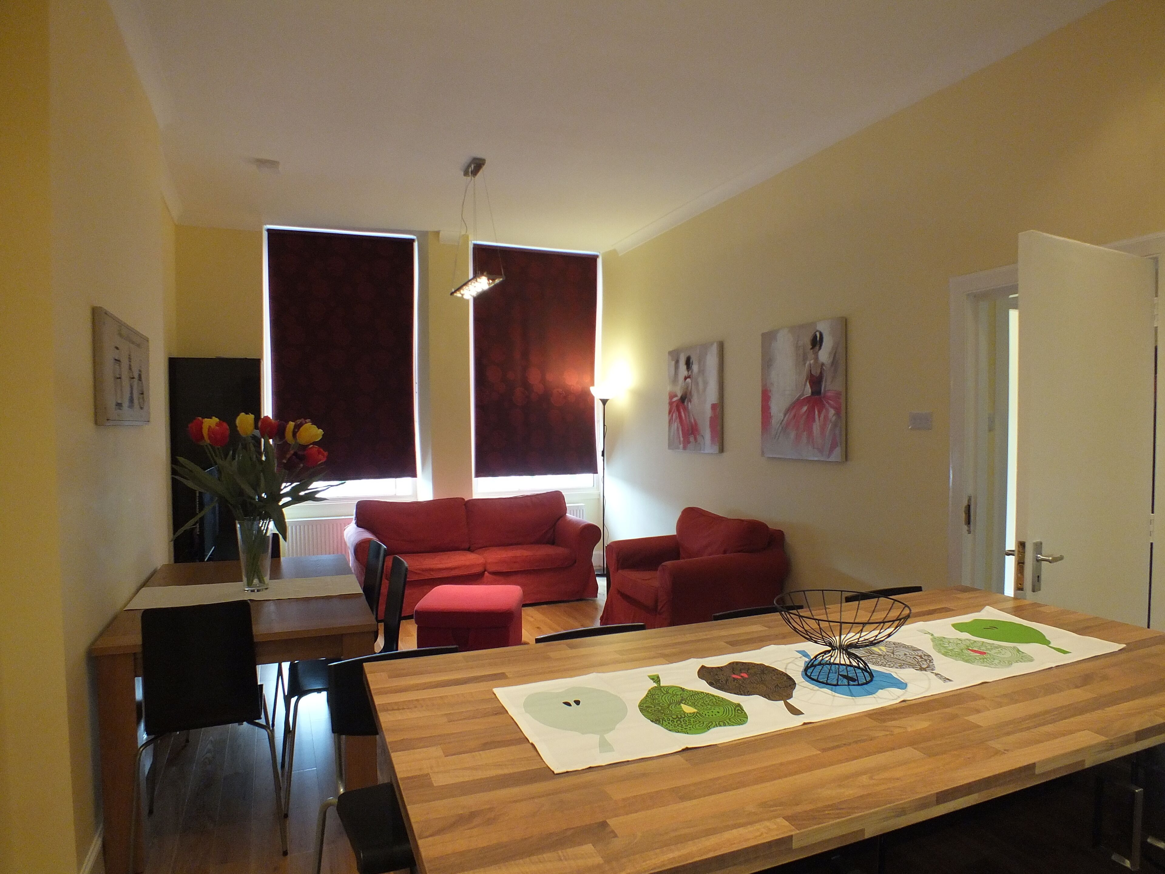 Un comedor con una mesa de madera, sillas rojas y un jarrón de flores.