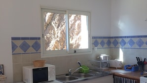 A compact kitchen with a washing machine, microwave, sink, and a window with a view of trees.