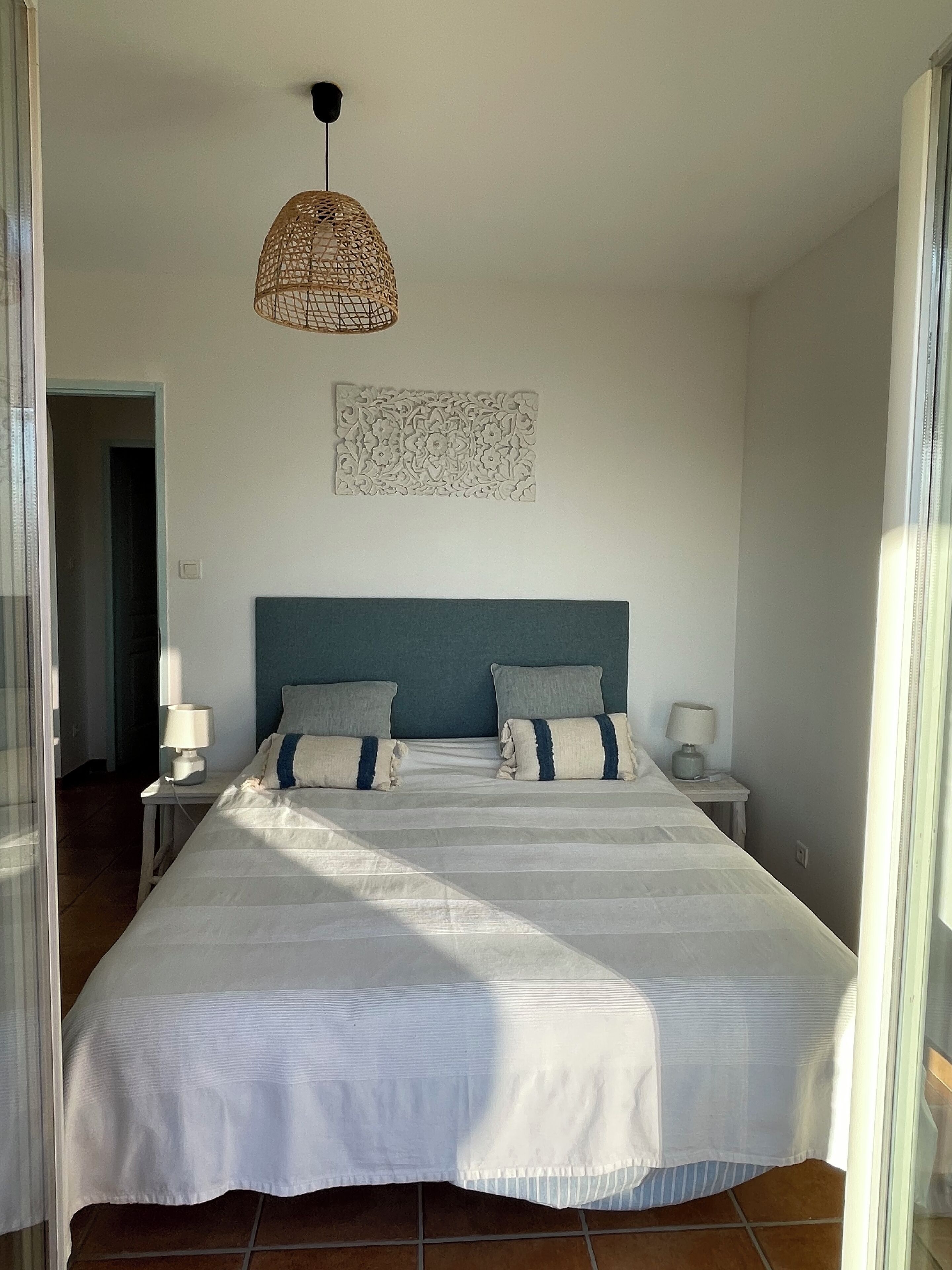 Camera da letto con un letto grande, due comodini con lampade, un elemento decorativo a parete e un lampadario in vimini.