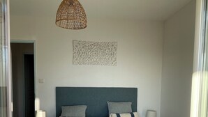 A bedroom with a large bed, two bedside tables with lamps, a decorative wall piece, and a woven ceiling light fixture.