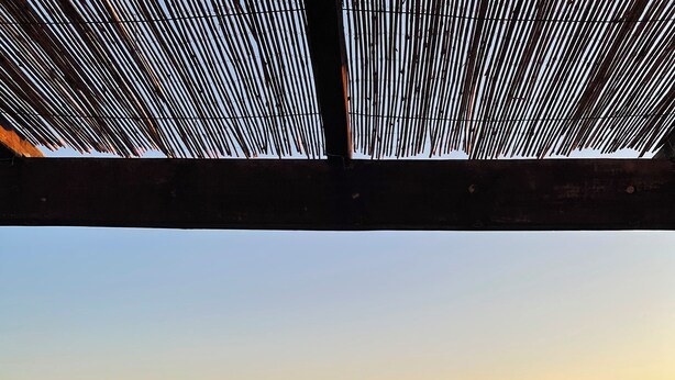A balcony with a view of a sunset over a body of water, surrounded by hills and trees.