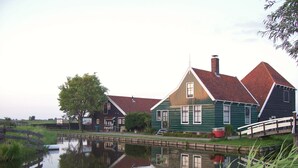 A traditional wooden house with a red roof, a small bridge, and a calm water body reflecting the house.