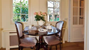 A dining room with a round table, four chairs, a vase with flowers, and a window with a view of greenery.