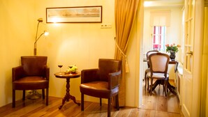 A room with two leather chairs, a small round table with a fruit bowl and wine glasses, a framed picture on the wall, and a door leading to another room.