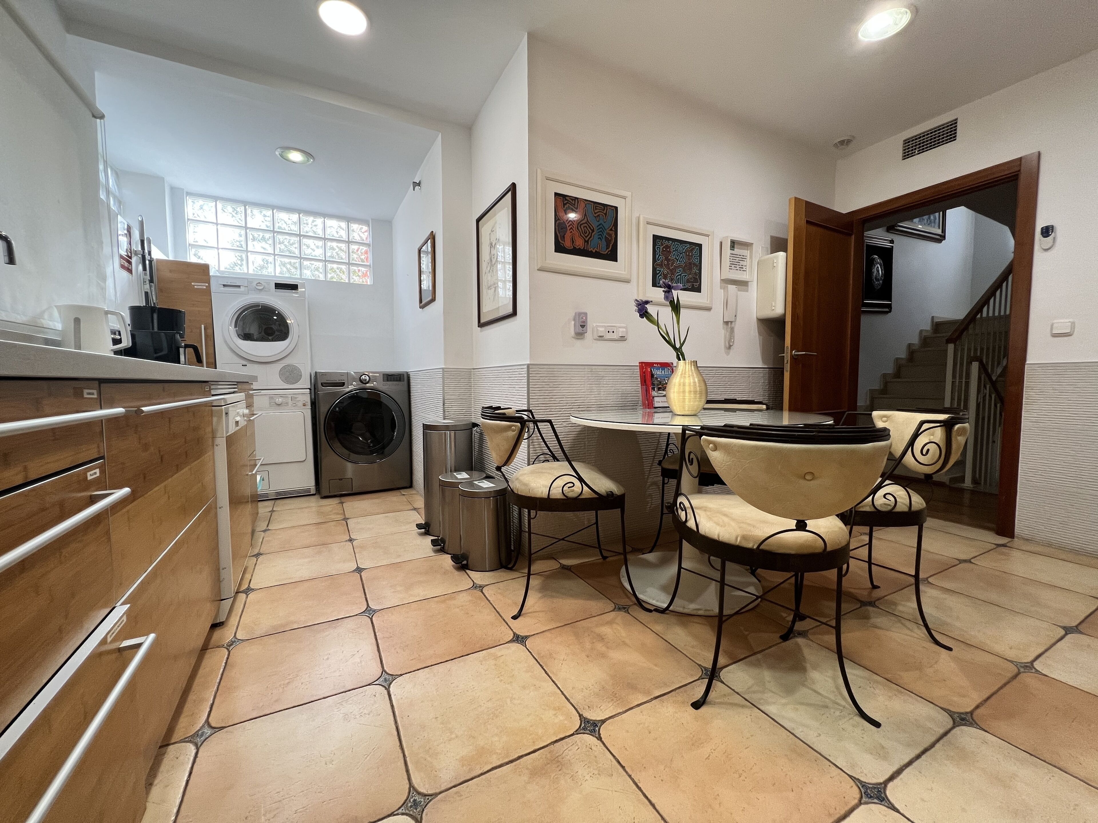 Uma cozinha compacta com máquina de lavar, um espaço de refeições com cadeiras e uma escada que dá acesso a outro nível.