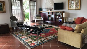 Un salon avec un canapé, un fauteuil et une table basse. On y trouve également une bibliothèque et un téléviseur fixé au mur.