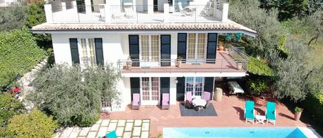 Una casa de dos pisos con piscina, mobiliario exterior y jardín.