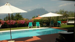 Une piscine entourée de chaises longues et de parasols, avec une végétation luxuriante et des montagnes en toile de fond.