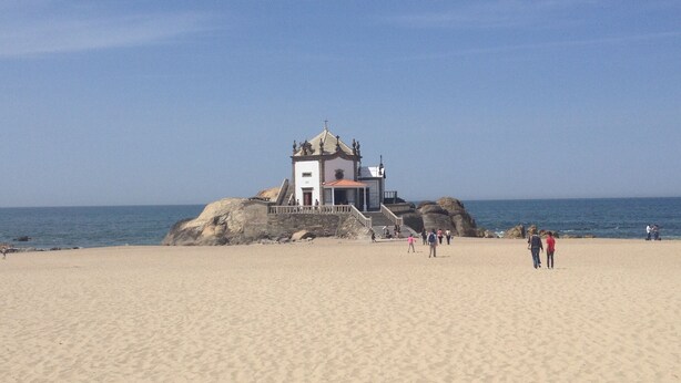 A beach with a small chapel on a rock, clear skies, and people walking. - Apartment in residence 50 meters from the beach and 500m from Miramar Golf (Vila Nova De Gaia)