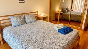 A bedroom with a bed, a nightstand with a lamp, a mirror, and a window with curtains. - Apartment in residence 50 meters from the beach and 500m from Miramar Golf (Vila Nova De Gaia)
