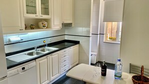 A modern kitchen with white cabinets, a black countertop, and a Bosch dishwasher. There is a small table with a bottle of wine, glasses, and a basket. - Apartment in residence 50 meters from the beach and 500m from Miramar Golf (Vila Nova De Gaia)