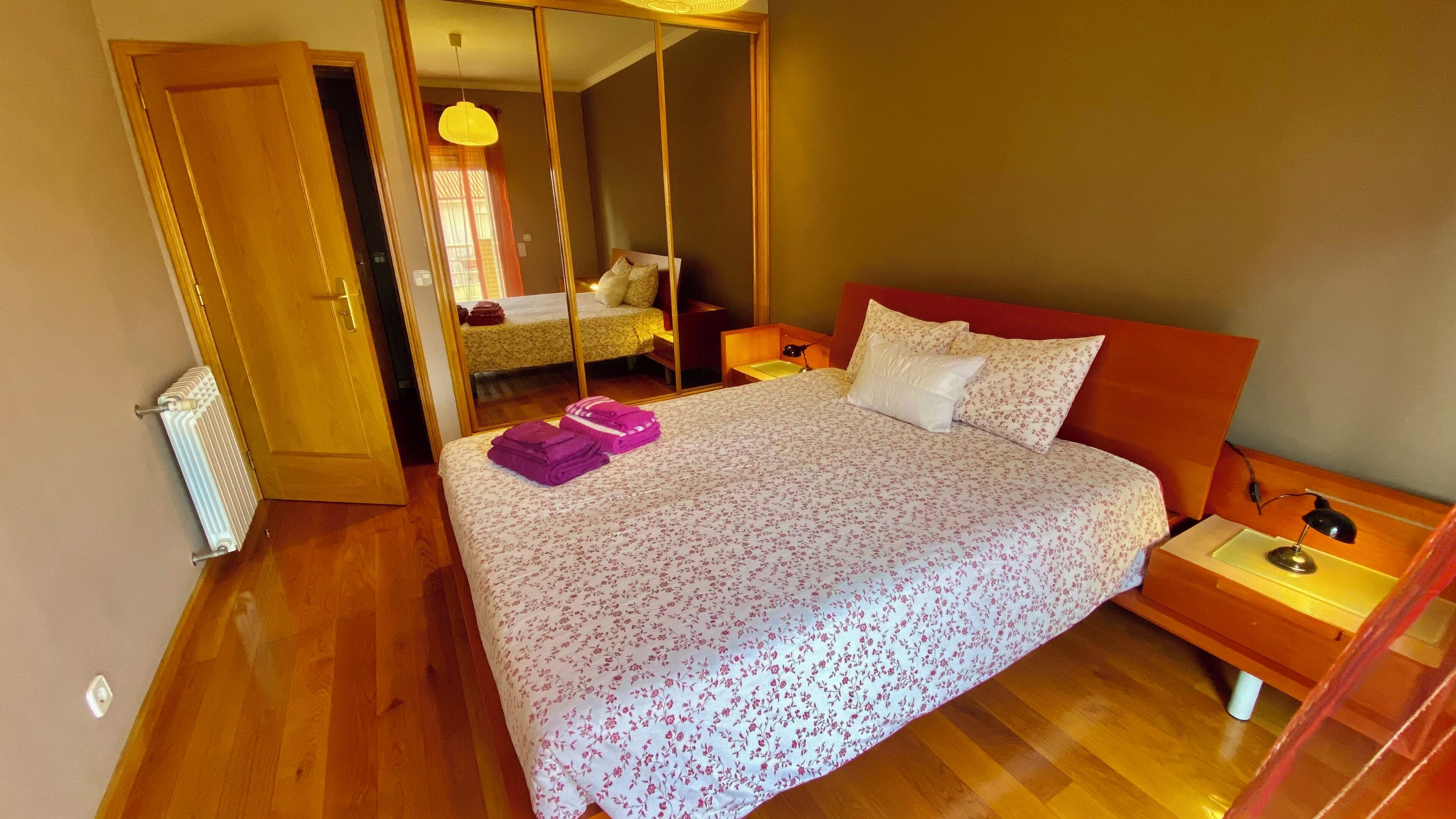 Un dormitorio con una cama, una mesita de noche, un espejo y piso de madera.