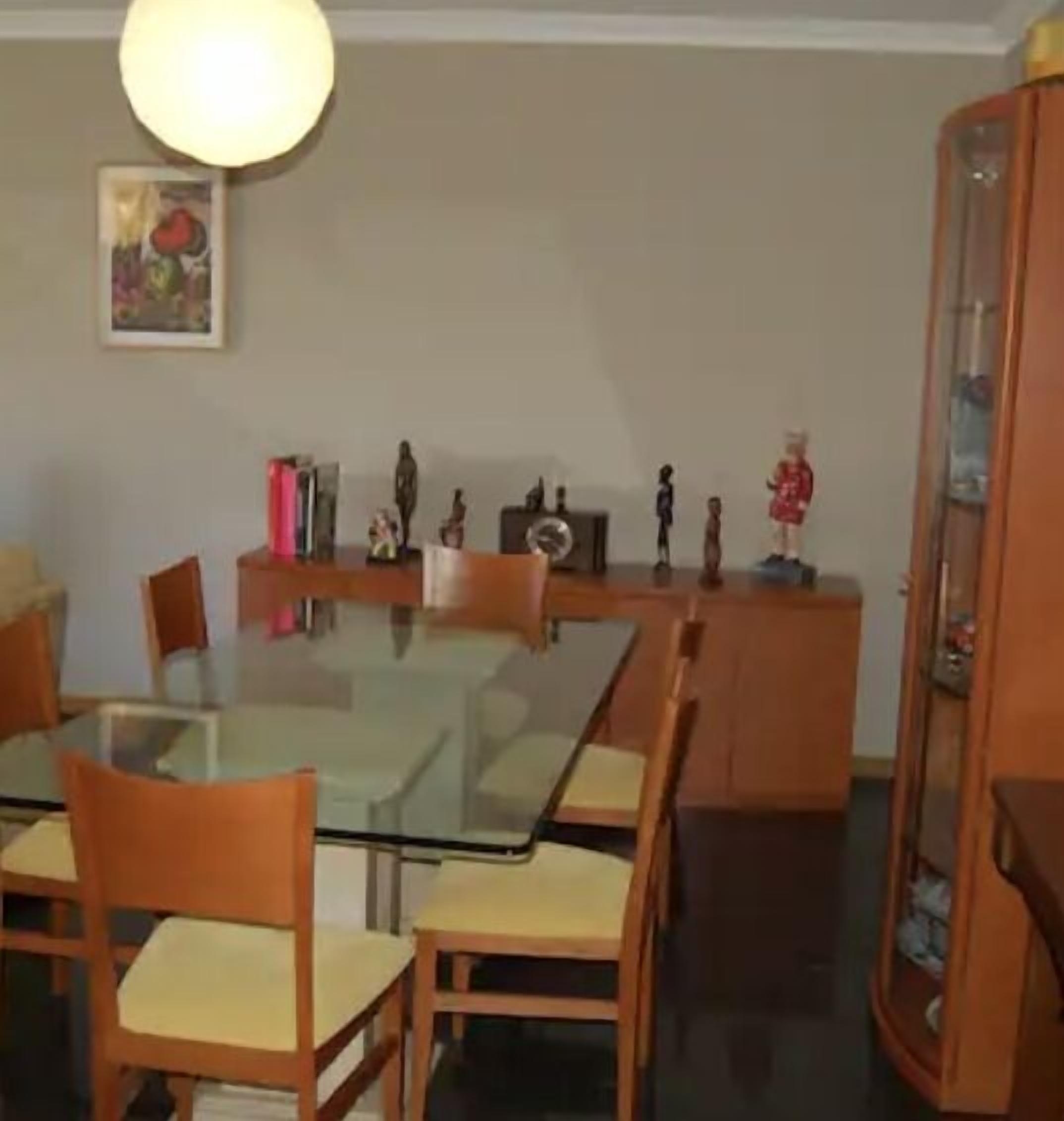 Ruokailutilassa on lasipöytä, jonka ympärillä on puisia tuoleja, koriste-esineitä sisältävä kaappi ja katosta roikkuva valaisin.
