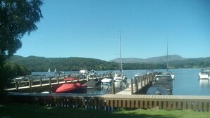 A marina with docked boats, a wooden pier, and a grassy area. - Log Cabin On Shores Of Lake Windermere, Surrounded By Breathtaking Scenery (Windermere)