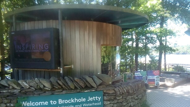 A wooden jetty structure with a sign welcoming visitors to Brockhole Jetty, indicating boats to Bowness, Lakeside, and Waterhead. - Log Cabin On Shores Of Lake Windermere, Surrounded By Breathtaking Scenery (Windermere)