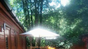 A wooden deck with a table and chairs, surrounded by a wooden railing, and potted plants. - Log Cabin On Shores Of Lake Windermere, Surrounded By Breathtaking Scenery (Windermere)