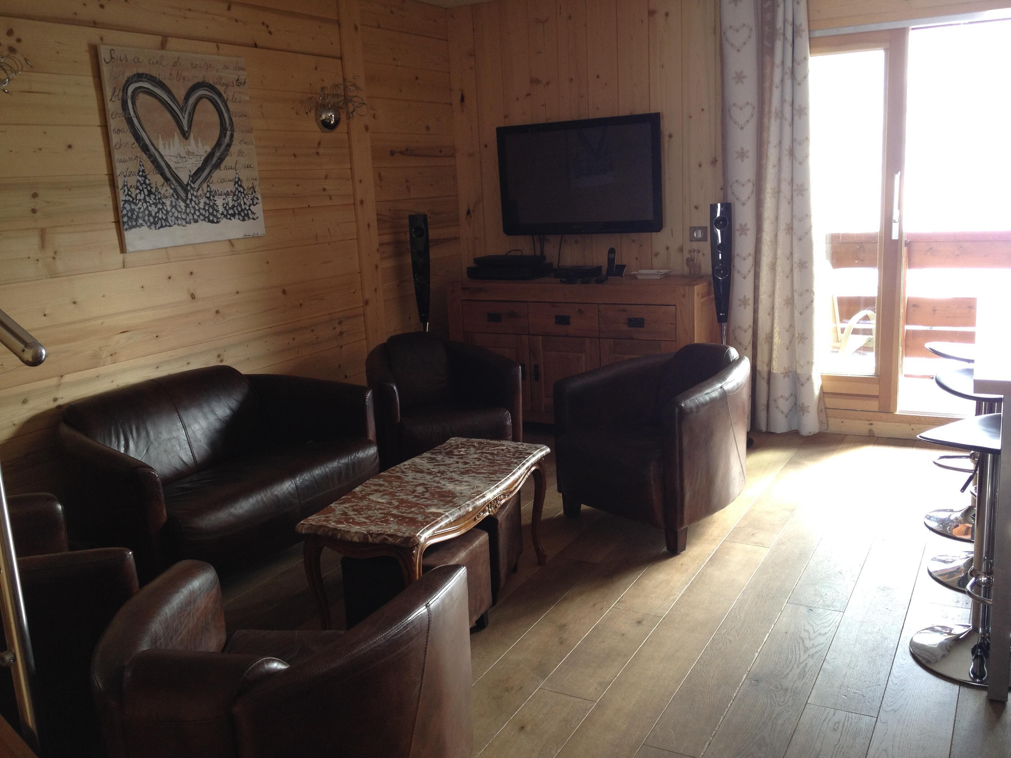 A wooden interior with a leather sofa, two armchairs, a small table, a TV, and a wooden cabinet.