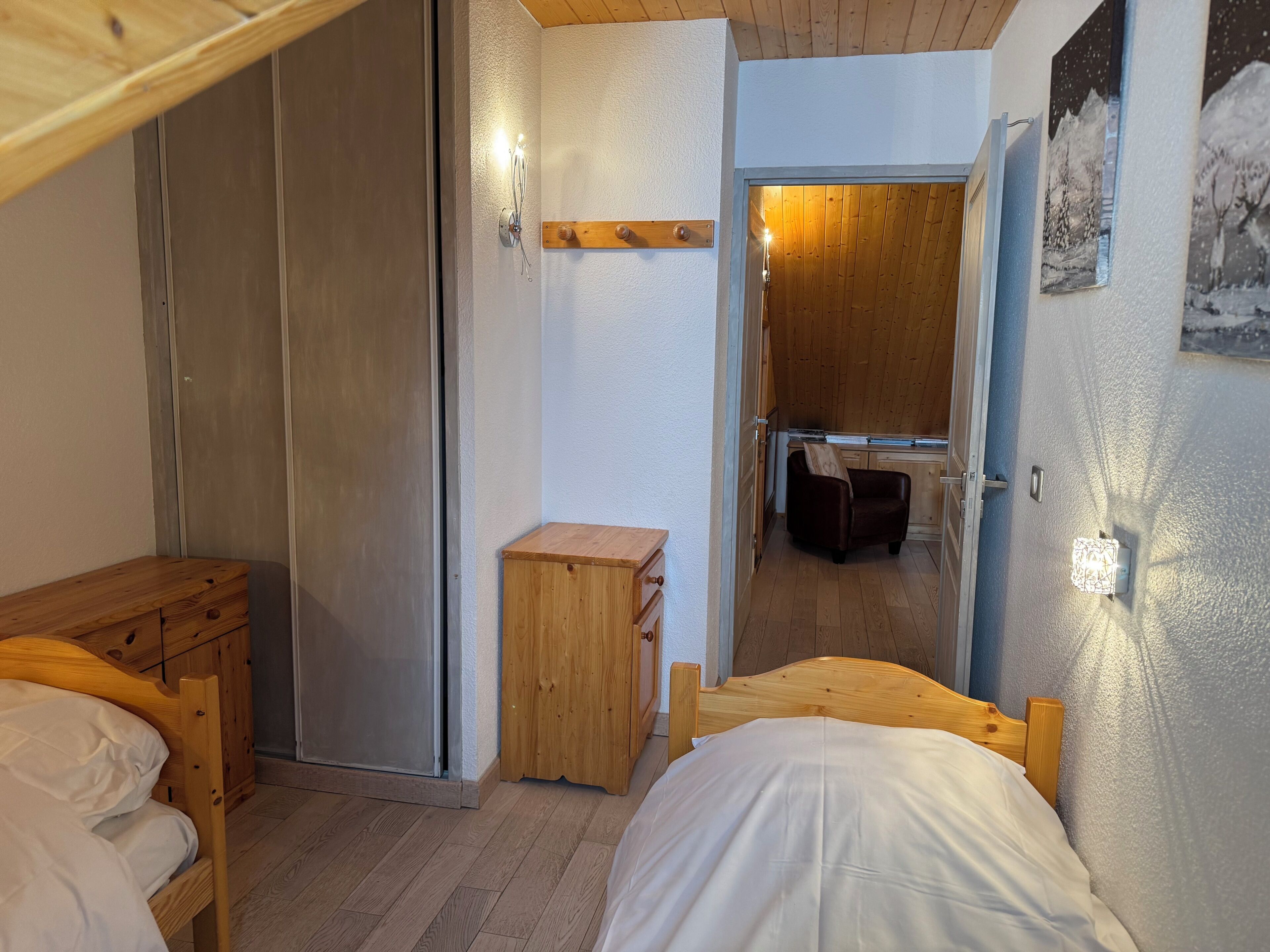 A bedroom with a bunk bed, wooden furniture, a small wooden cabinet, a mirror, and a bathroom visible through an open door.