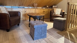 Et hyggeligt loftrum med træloft, et rundt spisebord, en sofa, en bænk og gelænder i træ.