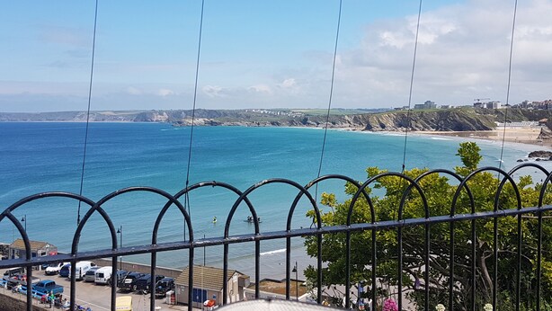 Vista costera con cielo despejado, playa y un estacionamiento con vehículos.