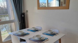 Un comedor con una mesa blanca, cuatro sillas blancas y vistas al exterior a través de un amplio ventanal.
