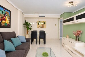 A modern living room with a sofa, coffee table, dining area, and a TV mounted on the wall.