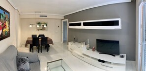 Un salon moderne comprenant un coin repas, un téléviseur à écran plat et un meuble de rangement blanc pour les appareils multimédias.
