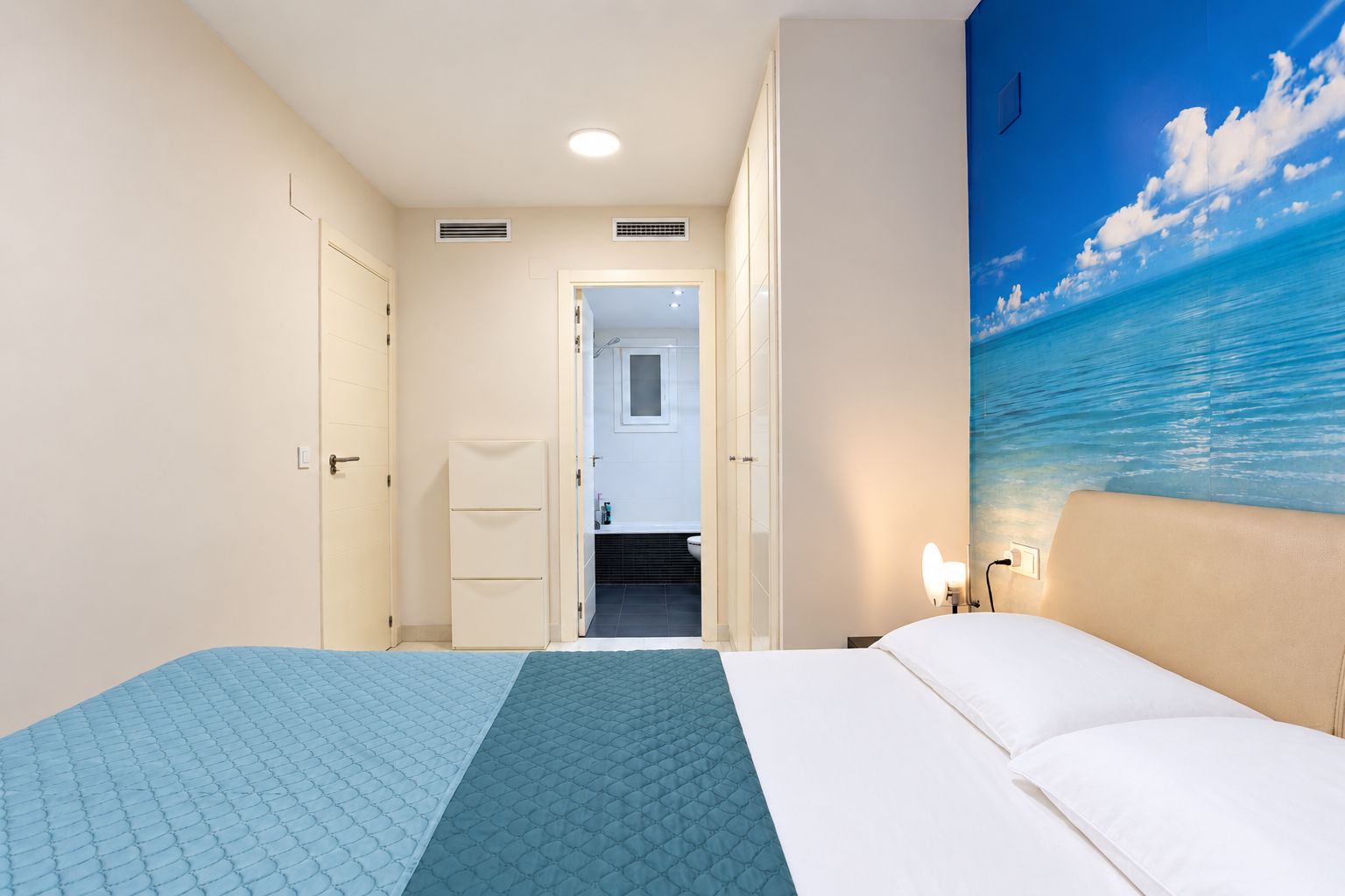 Une chambre d’hôtel avec un lit, une table de chevet, un mur orné d’un tableau et une porte donnant sur une salle de bain.